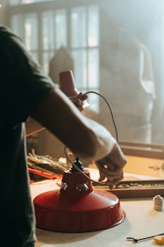 Photo by cottonbro studio Person repairing red lamp in sunlit workshop, showcasing craftsmanship and tools.