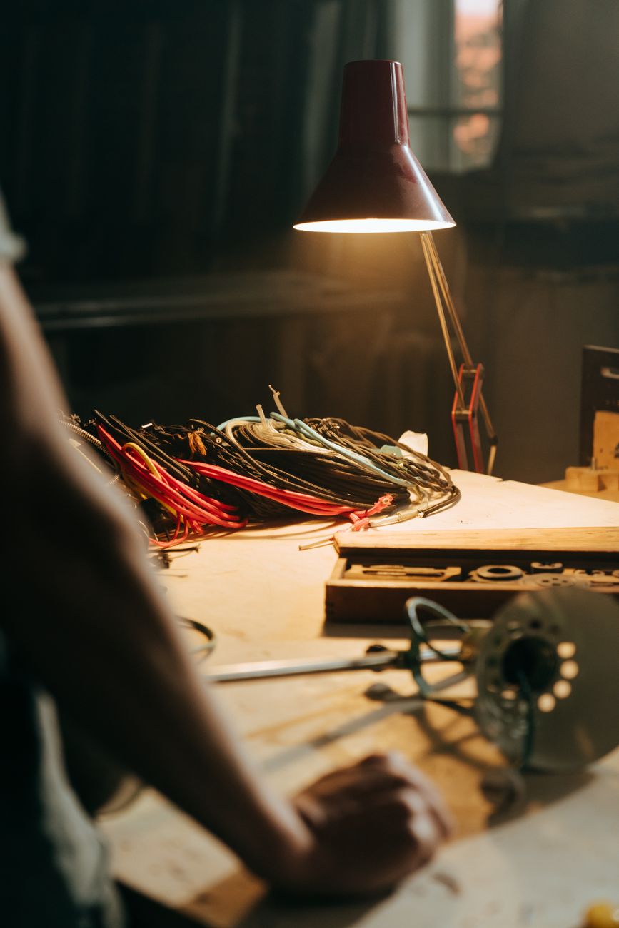 Warmly lit workshop with tools, wires, and a vintage lamp, perfect for crafts and repairs.