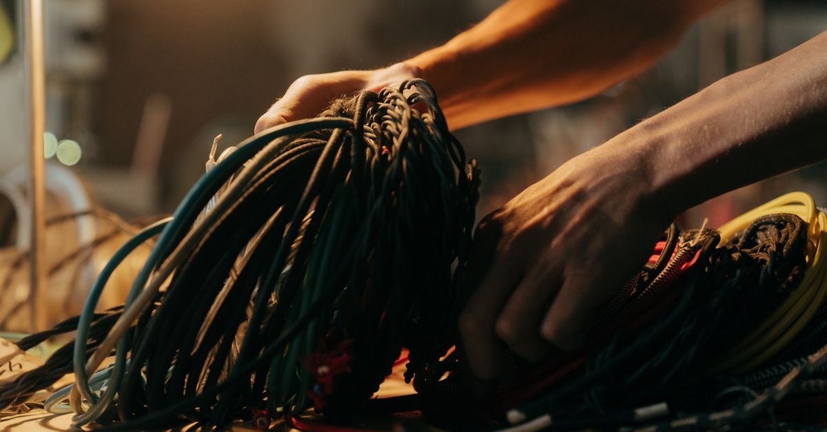 Hands sorting through a variety of colorful electrical wires on a table, illuminated by soft lighting.