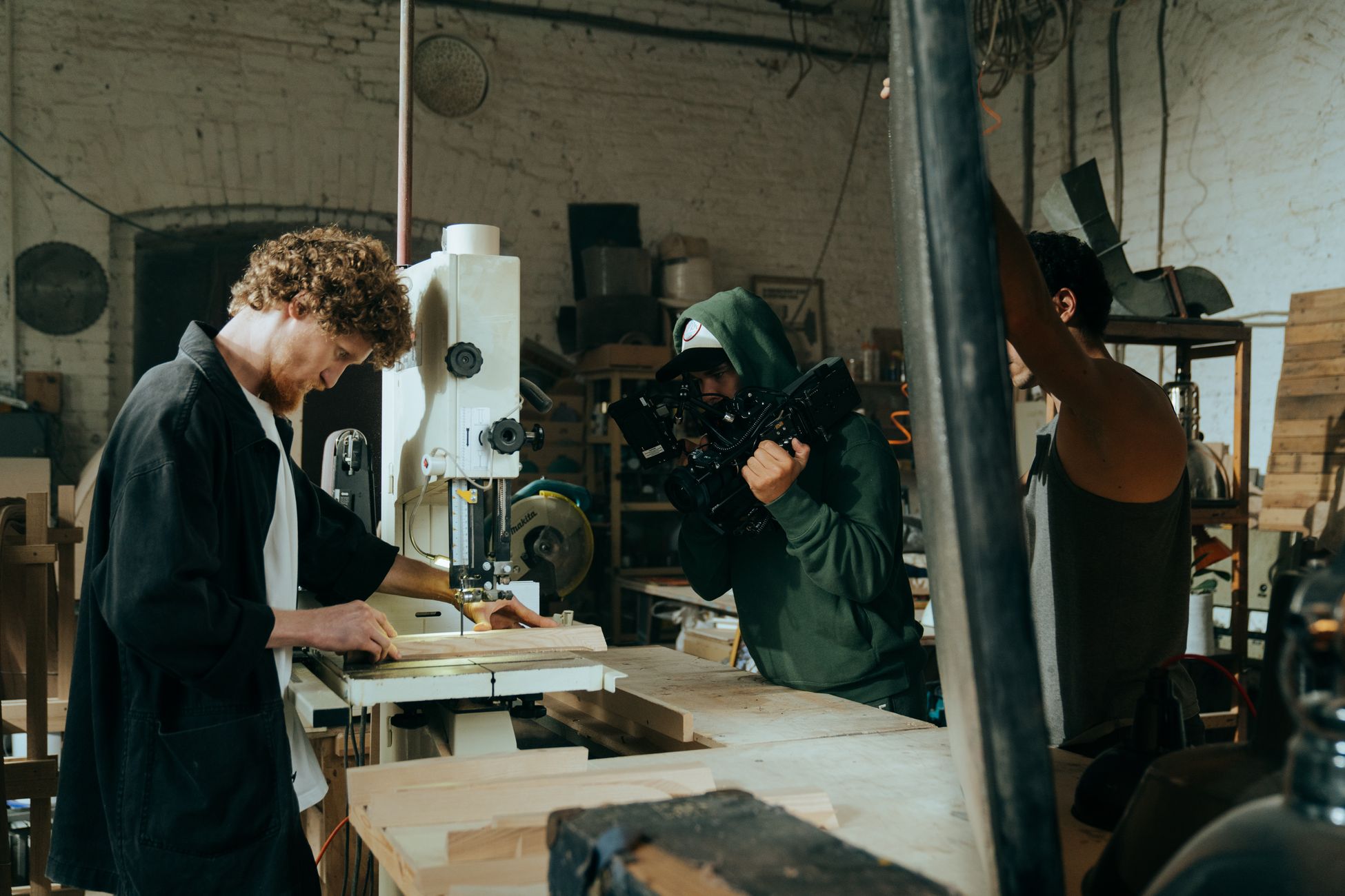 A craftsman working in a workshop is filmed by a crew using professional equipment.