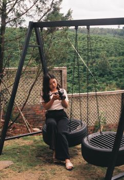 A woman sitting on a swing with a camera, enjoying the outdoor view in Lâm Đồng, Vietnam.