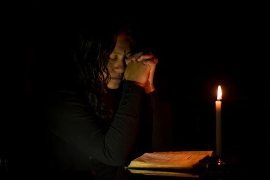 一个女人在烛光下深深沉浸在祈祷中，唤起一种宁静而沉思的心情