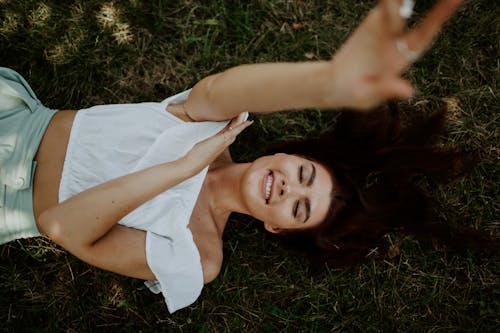 Woman in White Top Lying on Green Grass Field