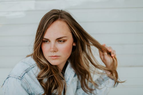 Selective Focus Photo of a Woman in a Blue Denim Jacket Touching Her Hair