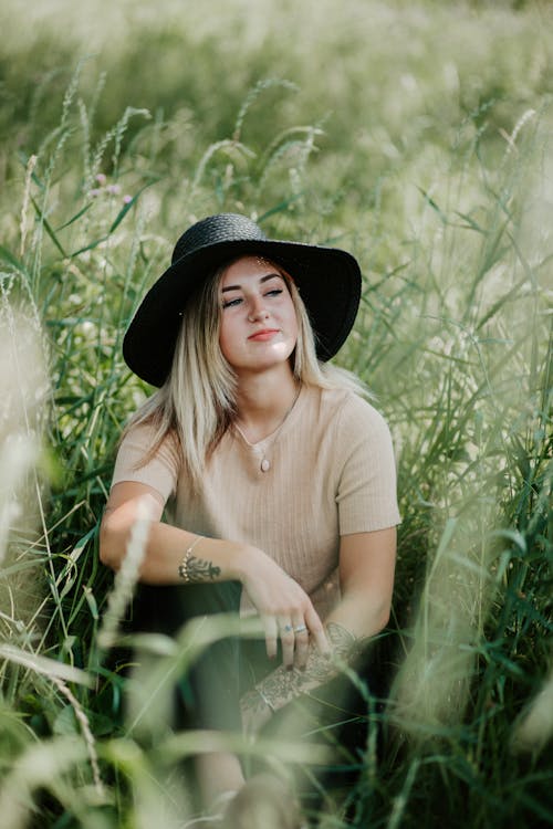 Photo of a Woman with a Black Hat Sitting on Green Grass