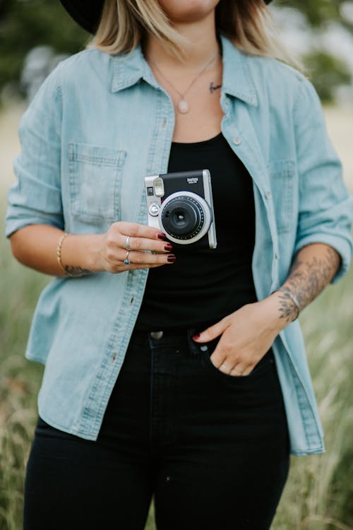 Donna In Giacca Di Jeans Blu Che Tiene Macchina Fotografica Nera E Argento