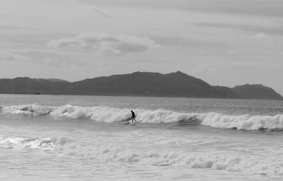 Black and white of lonely surfer riding surfboard on foamy waves of ocean against mountains