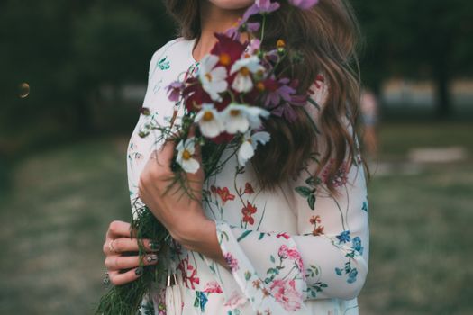一位身穿花裙的年轻女子在户外捧着五颜六色的花束，洋溢着春天的气息