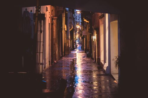 Free A moody alleyway with wet pavement illuminated by warm streetlights. Stock Photo