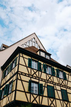 From below of half timbered house with yellow facade and small window on roof located in cloudy sky on street