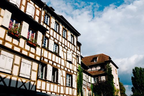 Free From below of old house with flowers and shutters on windows located on sunny street against cloudy sky in town Stock Photo