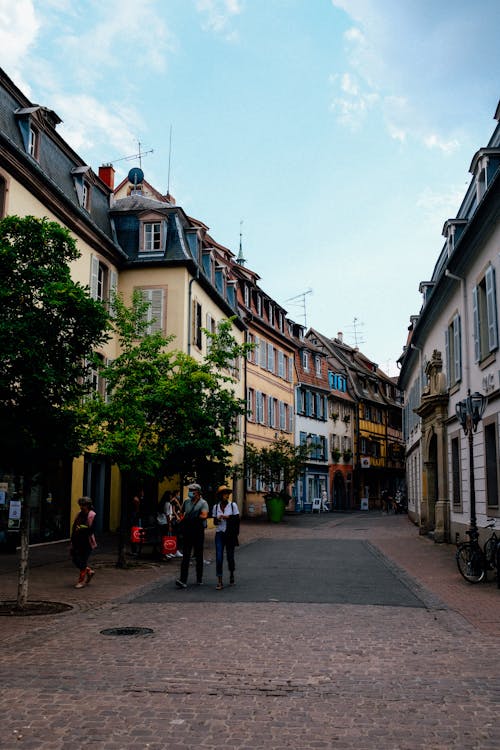 Unrecognizable travelers walking along narrow paved street between aged residential houses of historic district of Colmar