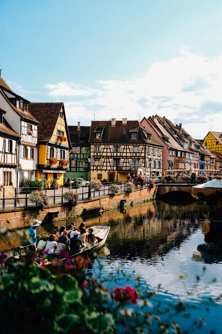 Tourists In Boat Floating On Canal Near Old Residential Houses