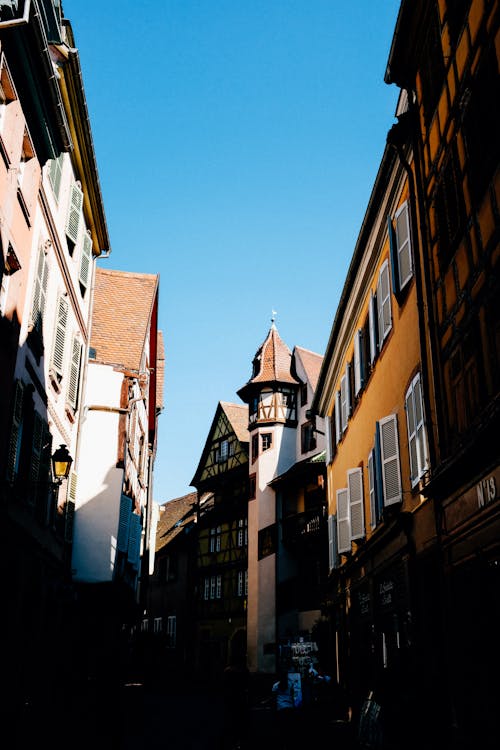 Narrow alley between typical old fashioned residential houses with windows and tower located against blue sky on sunny street in city