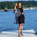 Full body of stylish lady in small black dress and high heeled sandals standing on berth near river and forest touching hair and closing eyes