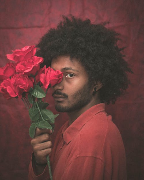 Close-Up Photo of a Man with Afro Hair Holding a Bunch of Red Roses