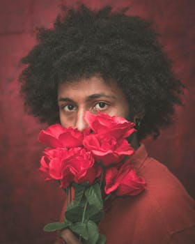 Artistic portrait of a person with roses, featuring afro hair in a studio setting.