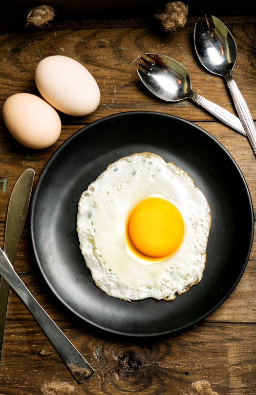 Overhead Shot of a Sunny Side Up Egg on a Black Plate