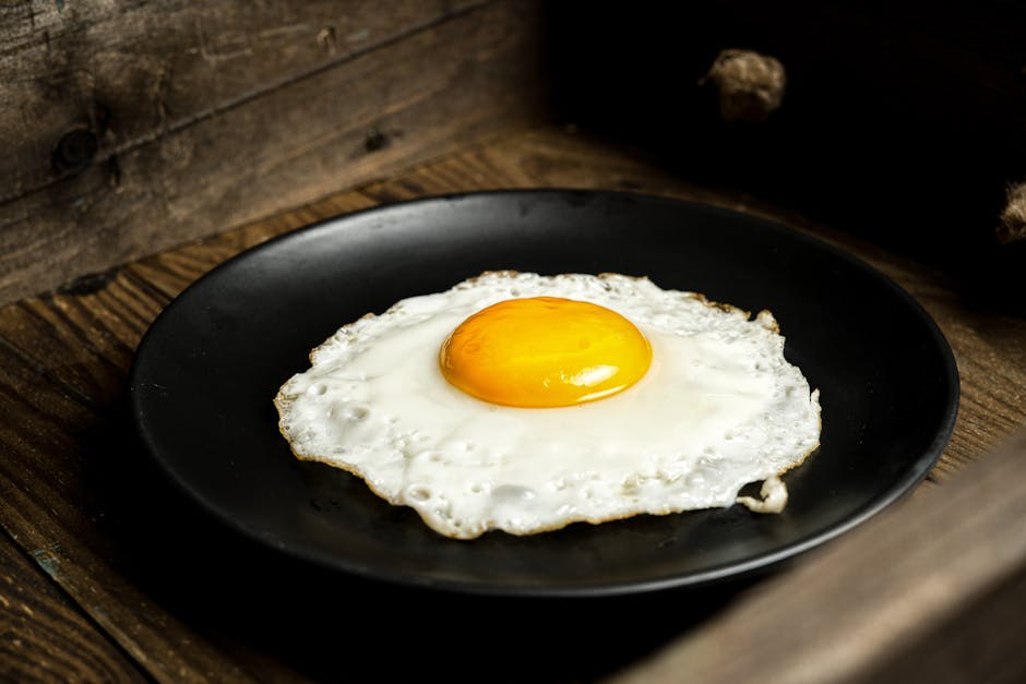 Close-up of a sunny-side up egg on a black plate with a rustic wooden background.