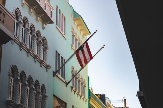 Street view of a vibrant building with architectural details and a flag under a clear sky.