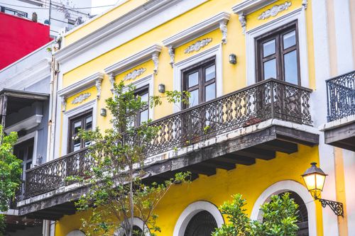 Free Vibrant yellow townhouse with ornate iron balcony and classic architectural details. Stock Photo