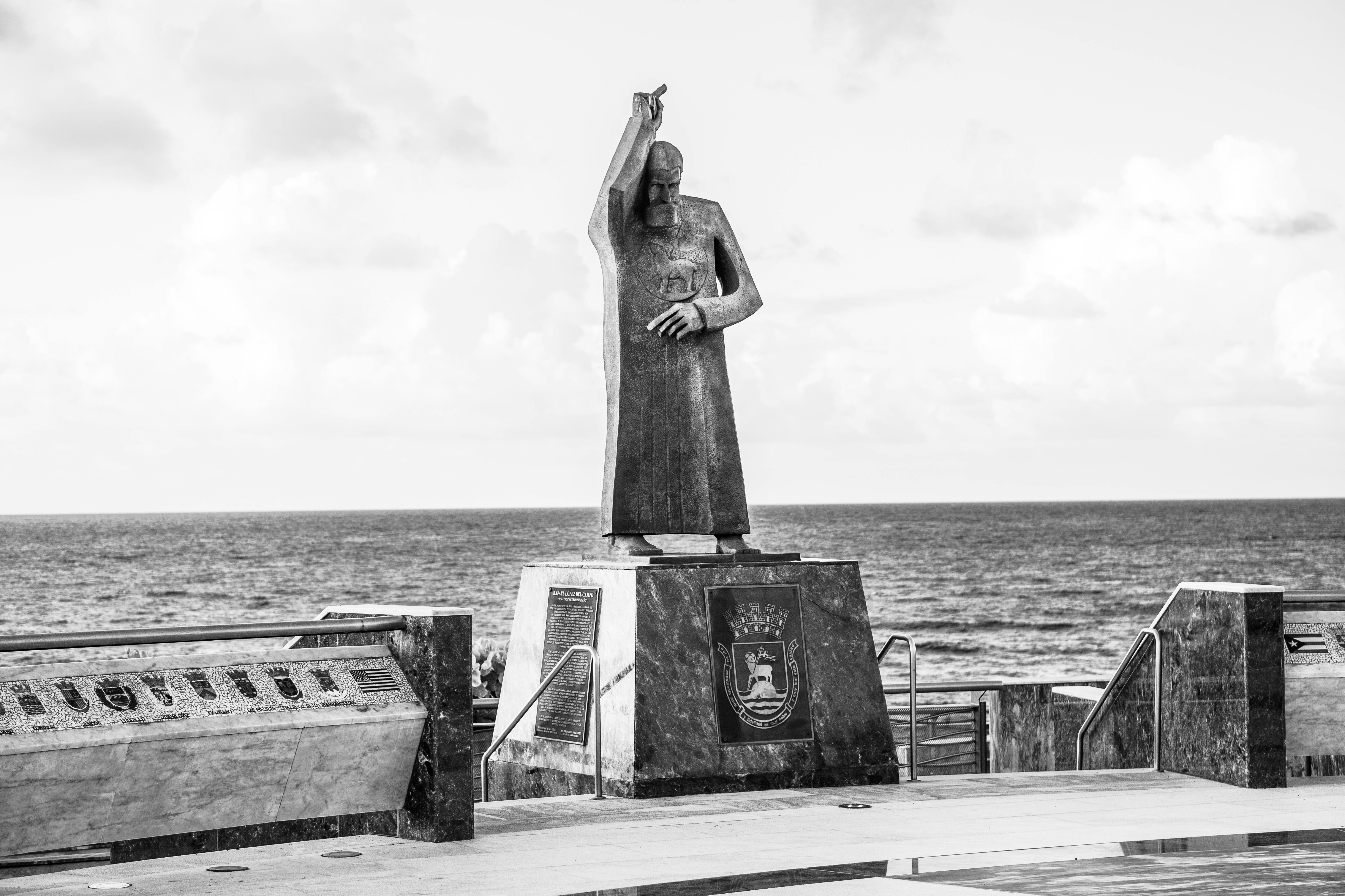 grayscale photo of statue of woman on concrete bench by the sea