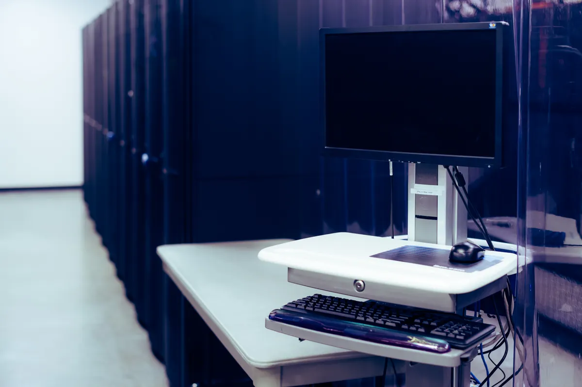 A data centre aisle of black server cabinets with a console cart holding a monitor and keyboard, where a VPS keeps Trader Workstation running for an IBKR strategy