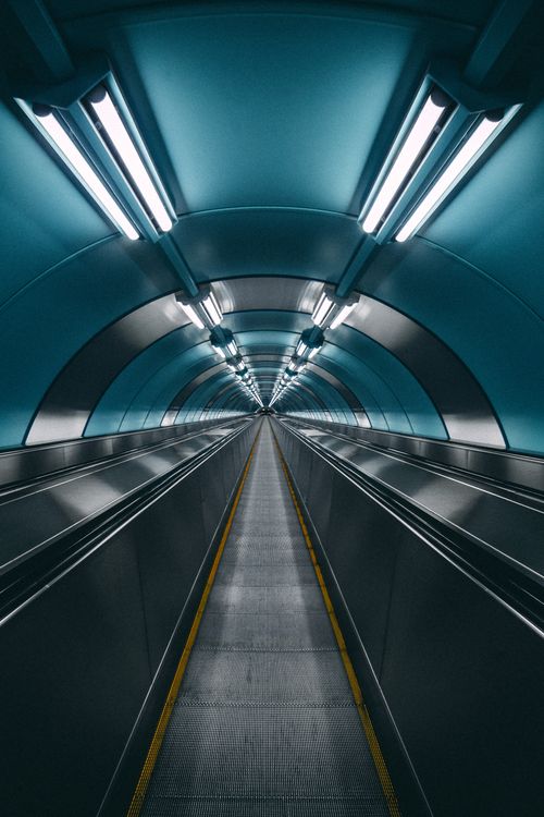 Free A modern, fluorescent-lit underground tunnel with a moving walkway, conveying urban innovation. Stock Photo