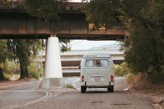 A classic Volkswagen camper van travels under a rural bridge, evoking nostalgia for road trips.