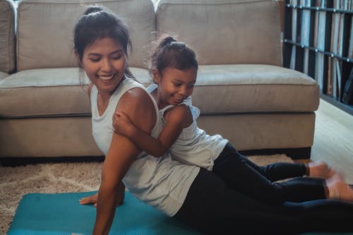 Happy ethnic girl lying on mothers back performing Cobra Pose