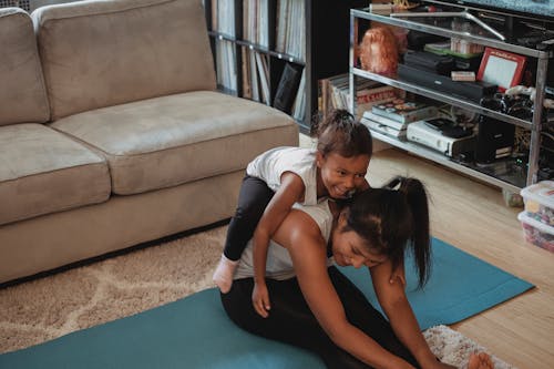 Funny kid lying on mothers back stretching body at home