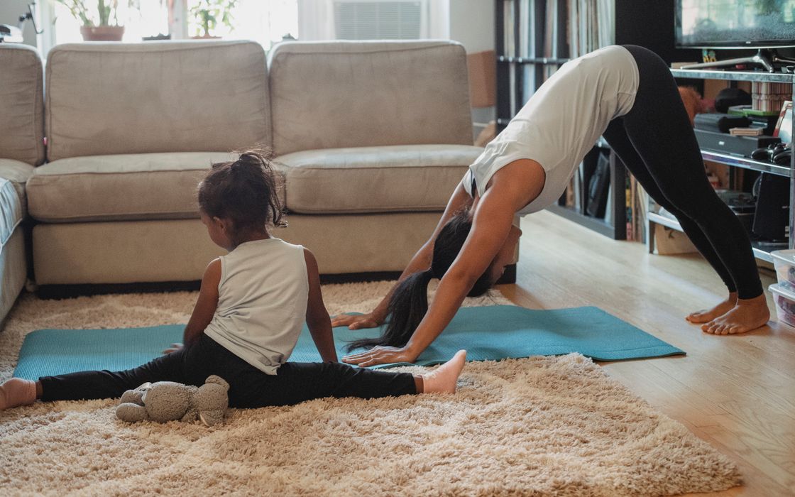 Unrecognizable female and little girl in sportswear stretching on carpet and stretch mat in living room