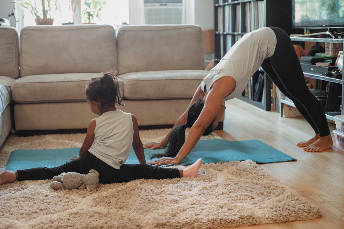 Free Unrecognizable female and little girl in sportswear stretching on carpet and stretch mat in living room Stock Photo