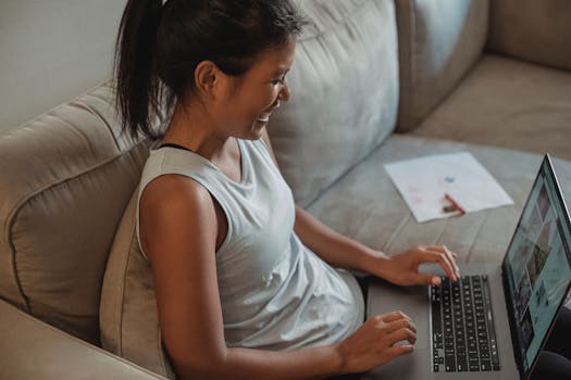 Smiling woman comfortably using laptop on sofa at home, casual and relaxed atmosphere.