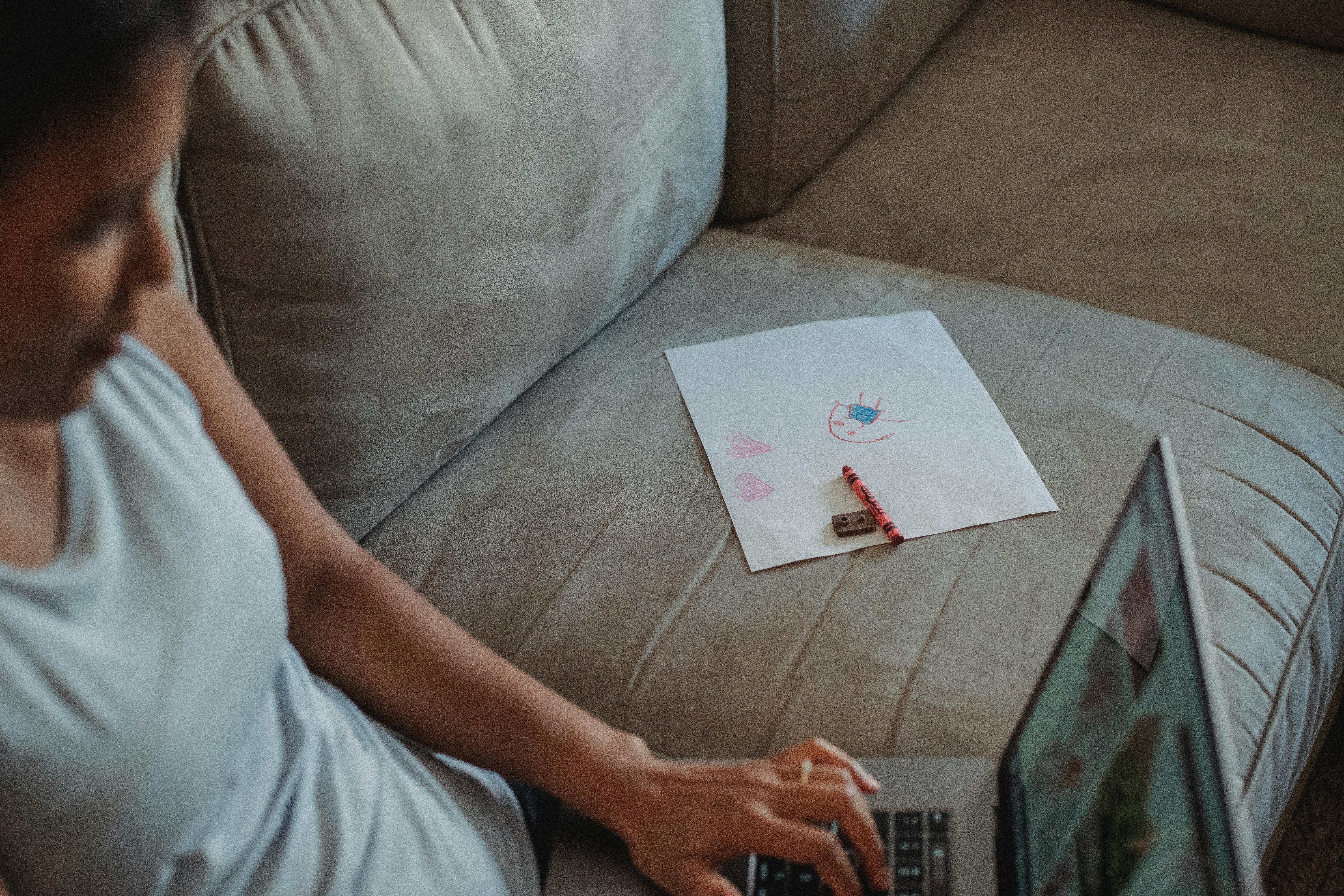 ethnic lady working on laptop near child painting on sofa