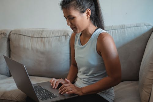 Free Adult lady sitting on sofa and using computer for remote work in living room while wearing casual outfit Stock Photo