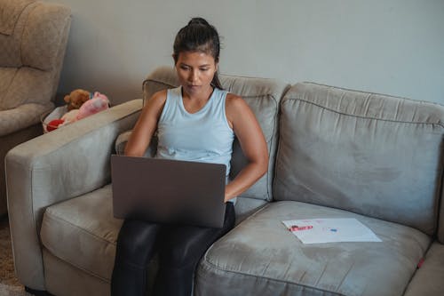 Ethnic female freelancer using computer near kid drawing on couch