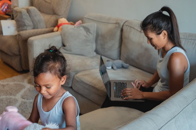 Ethnic Woman Working On Computer While Child Playing