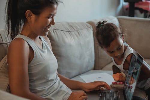 Free Hispanic mother and daughter using laptop on sofa Stock Photo