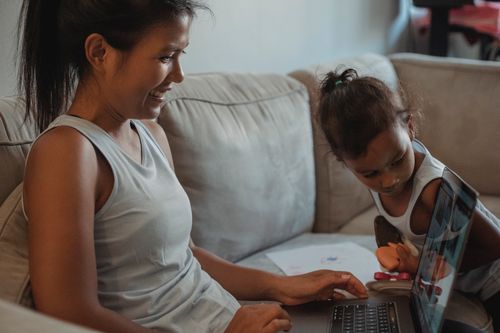 Free Woman with child surfing through computer on sofa while wearing casual outfit in living room Stock Photo