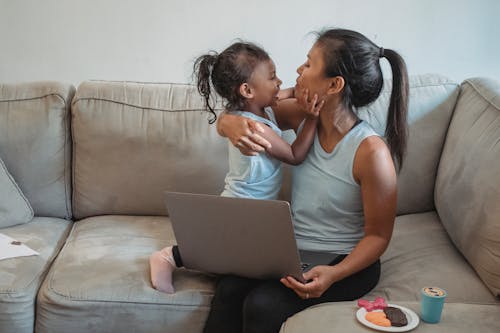 Young Asian mother with little daughter cuddling while watching video on laptop