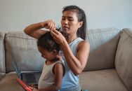Concentrated Hispanic female in casual clothes braiding adorable little daughter playing with toy