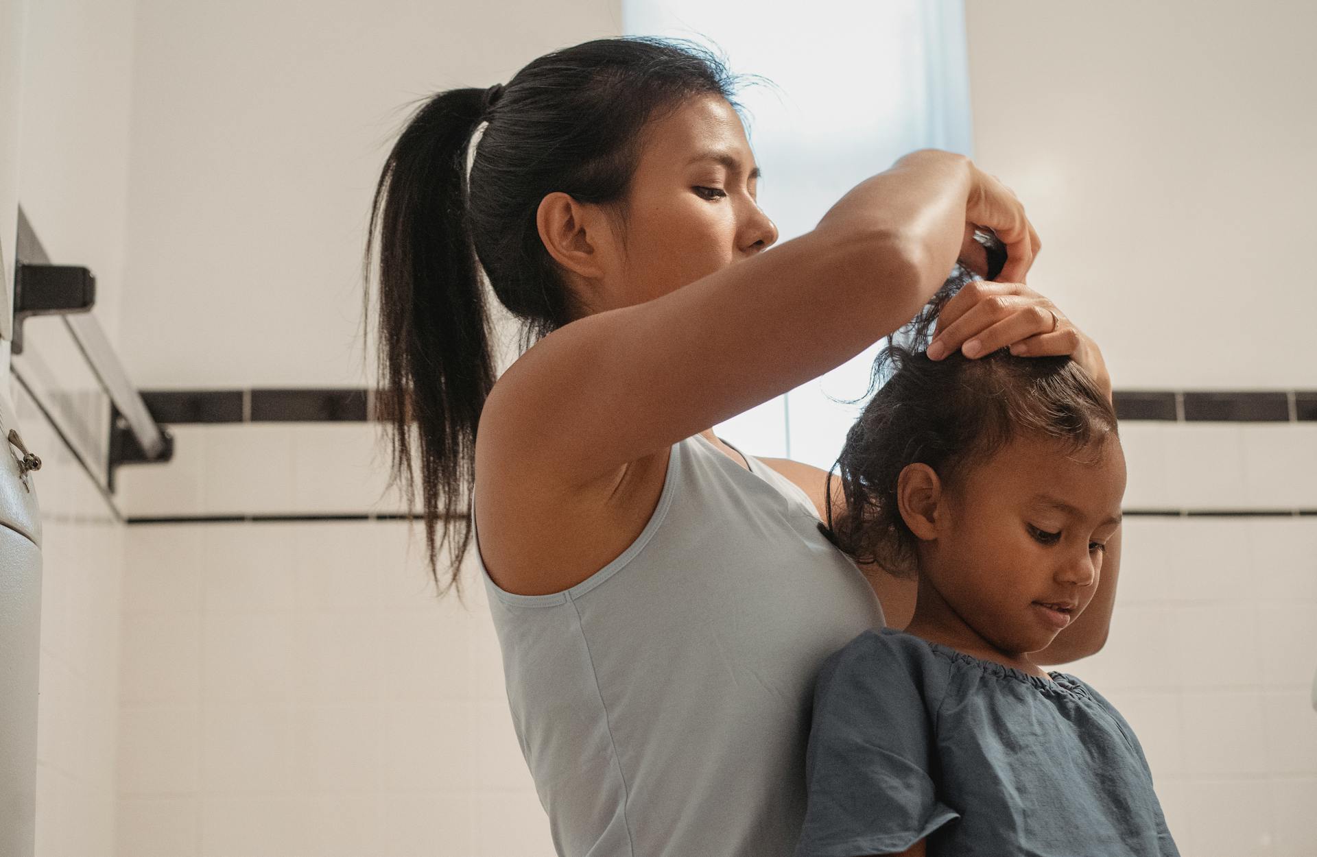 Side view of focused young Hispanic female in casual wear making hairdo for little daughter