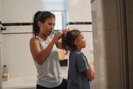 Side view of young Hispanic female in casual outfit standing in bathroom and braiding little daughter
