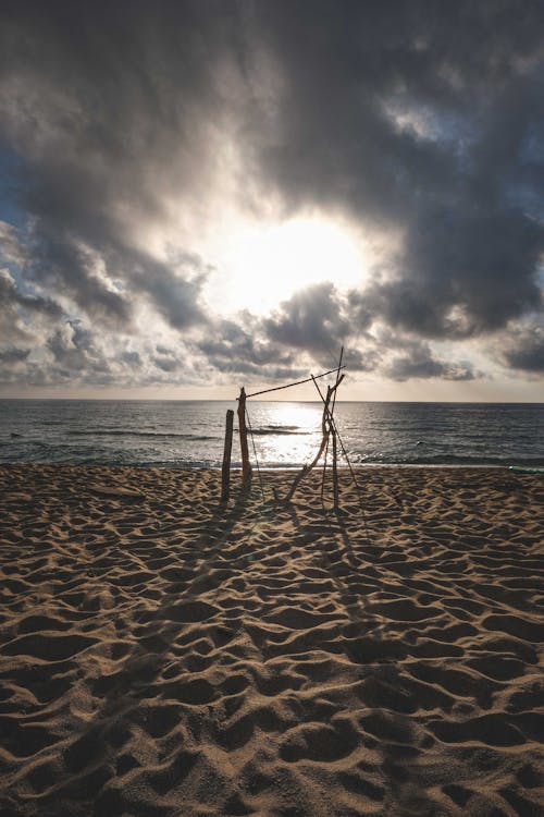 Scenery of wooden construction on sandy seashore near calm rippling sea beneath cloudy sky in early evening