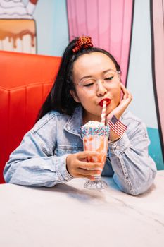 一位穿着牛仔夹克的女人正在一家装饰充满活力的复古主题餐厅里品尝洒在上面的奶昔