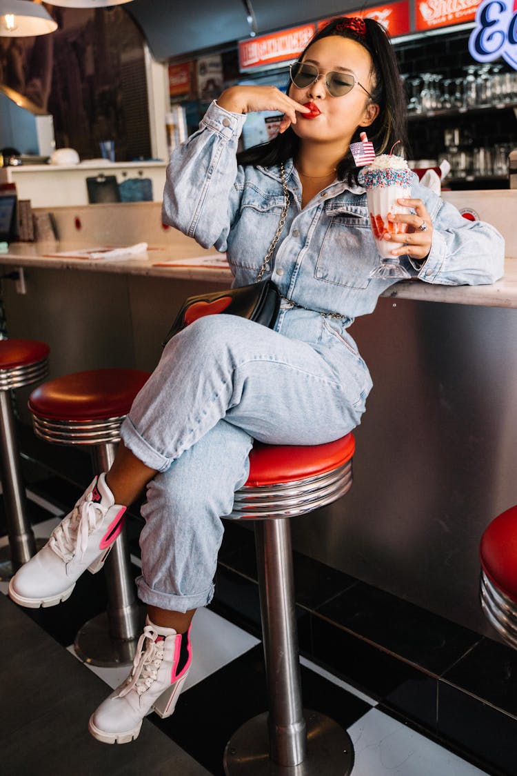 A Woman Sitting On A Diner Stool Holding A Milkshake
