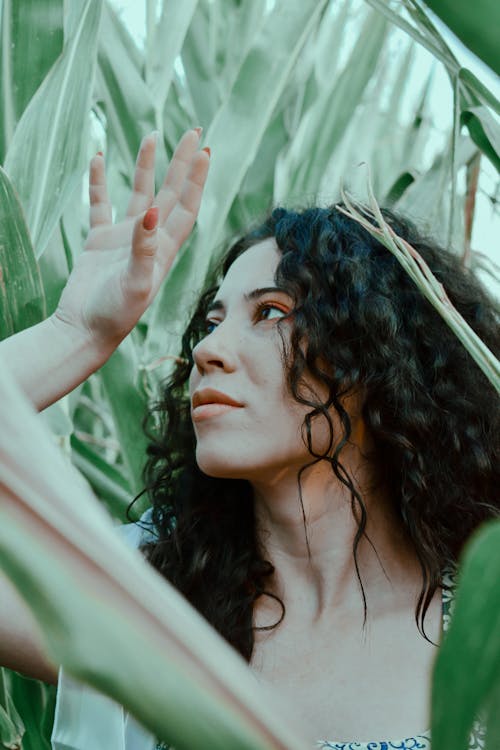 Feminine young brunette standing amidst tall green plants in garden