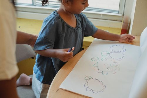 Free Crop concentrated cute little girl drawing flowers with wax crayons sitting at table Stock Photo