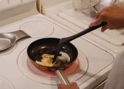 Crop unrecognizable person near white stove with black spatula cooking scrambled eggs in kitchen